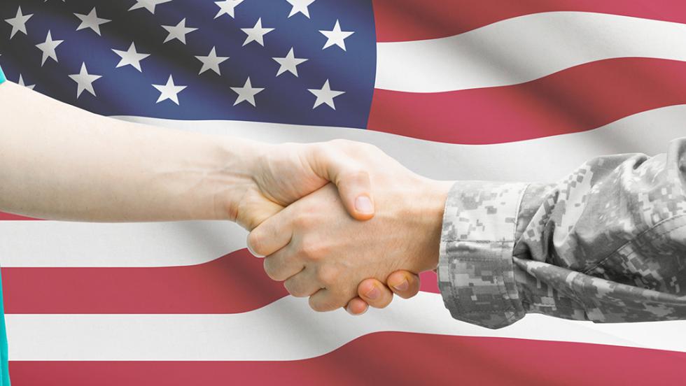 A physician and veteran shake hands in front of an American flag.